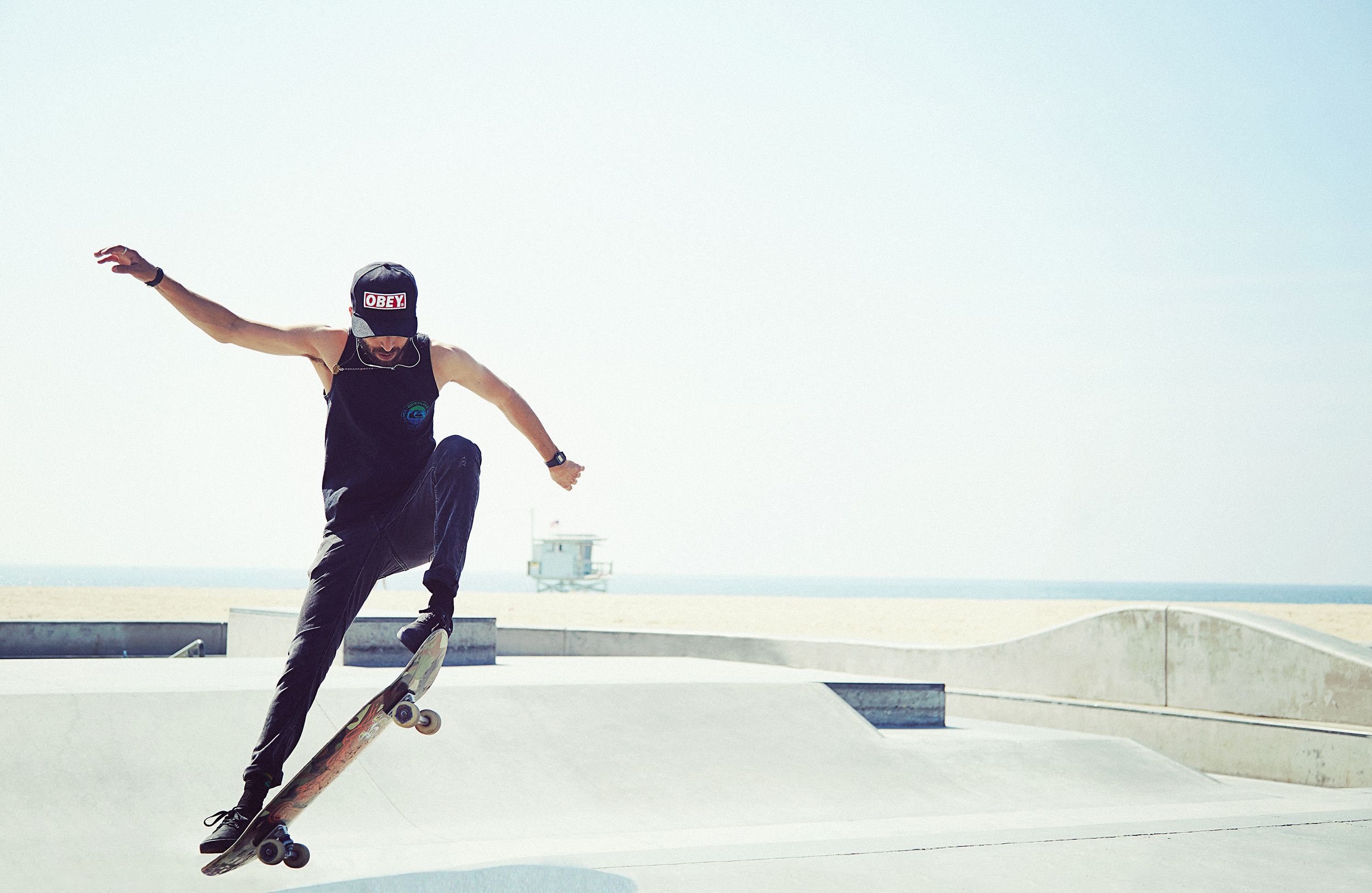 A man skateboards at a park with a beach visible in the background.