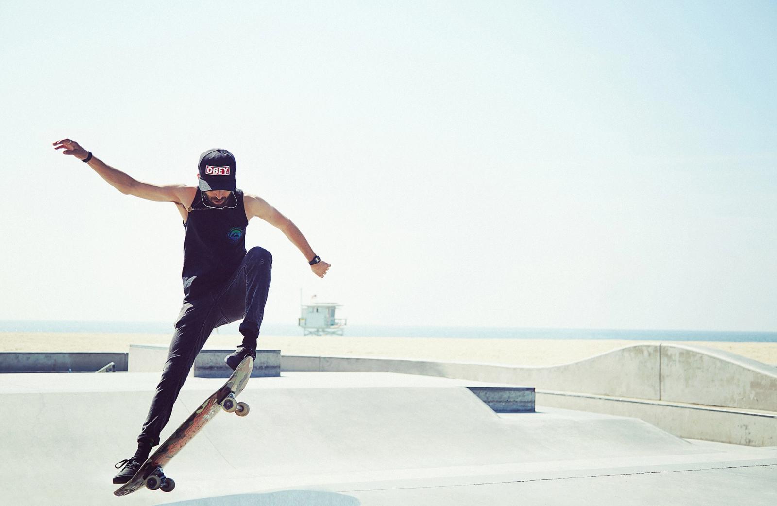 A man skateboards at a park with a beach visible in the background.