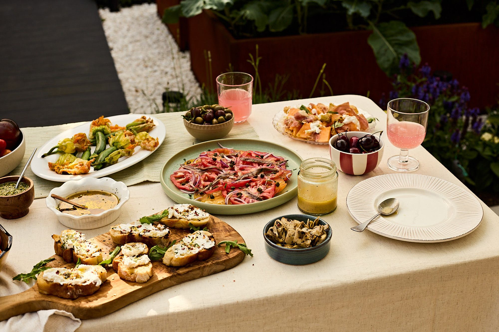 A table set with a variety of Italian-inspired dishes, including bruschetta, caprese, and pasta, in a garden or outdoor setting.