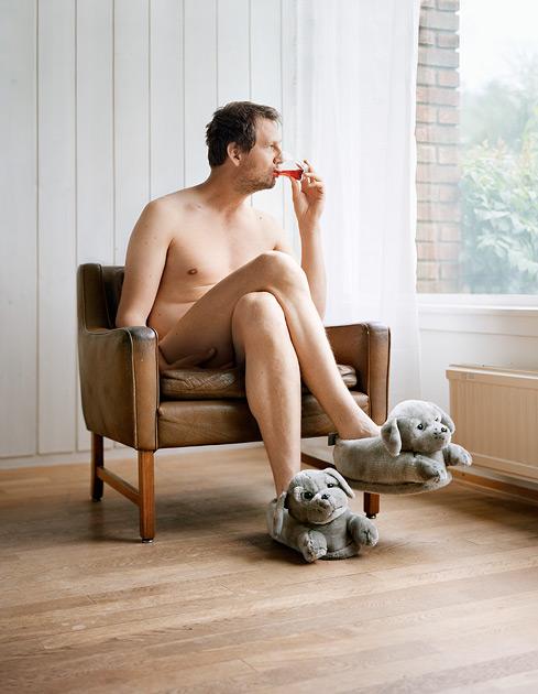 A man sitting in a chair, naked, with a phone in his hand, wearing no other clothing.