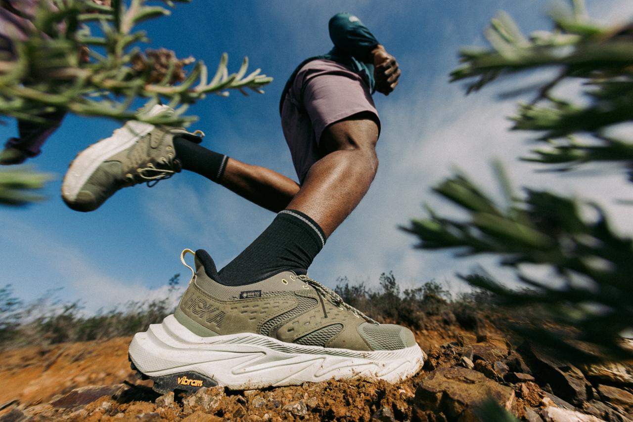 A person running in a desert landscape, wearing a pair of running shoes and a hat.