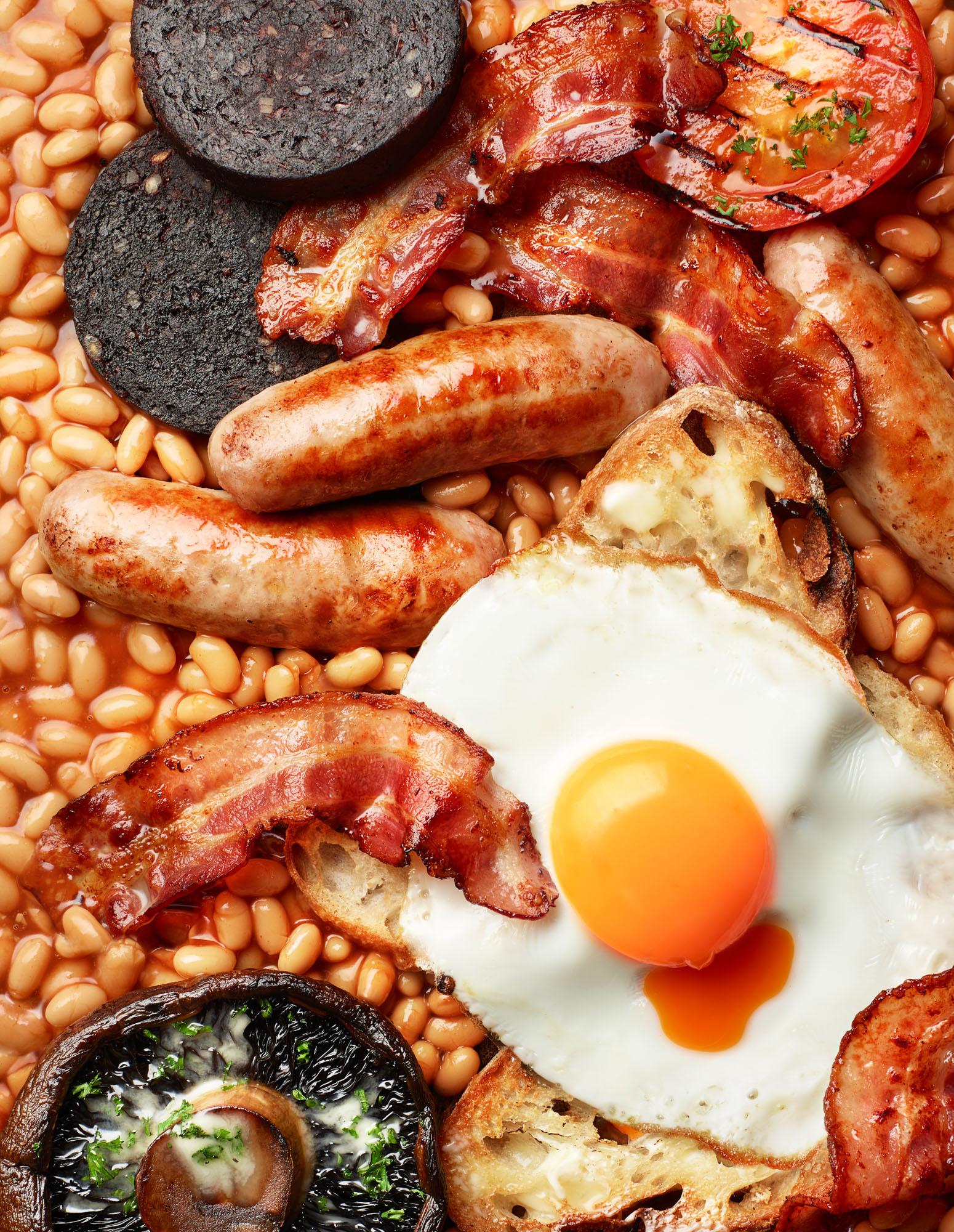 A close-up of a full English breakfast including eggs, sausages, bacon, beans, and toast.