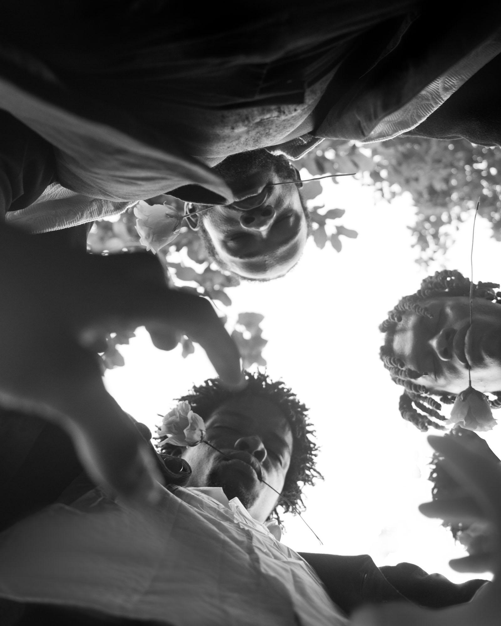 A group of people, likely friends or family, are looking up at the camera with smiles on their faces, surrounded by trees and foliage.