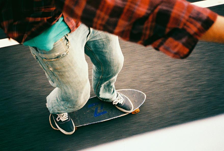 A person is skateboarding on a flat, smooth surface, wearing a red and black plaid shirt, blue jeans, and black and white sneakers.