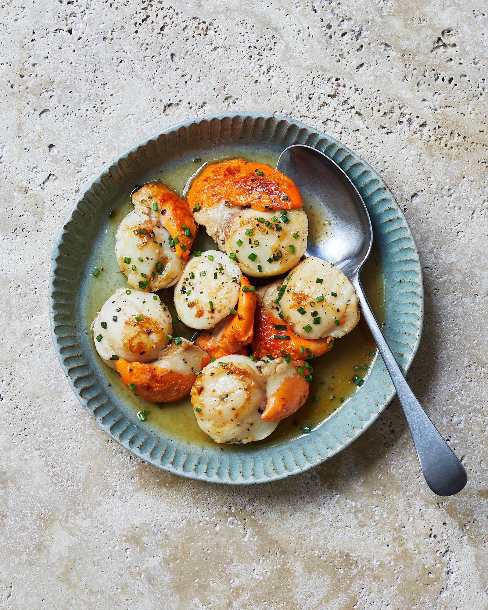 A plate featuring pan-seared scallops with sauce and fresh herb garnish.