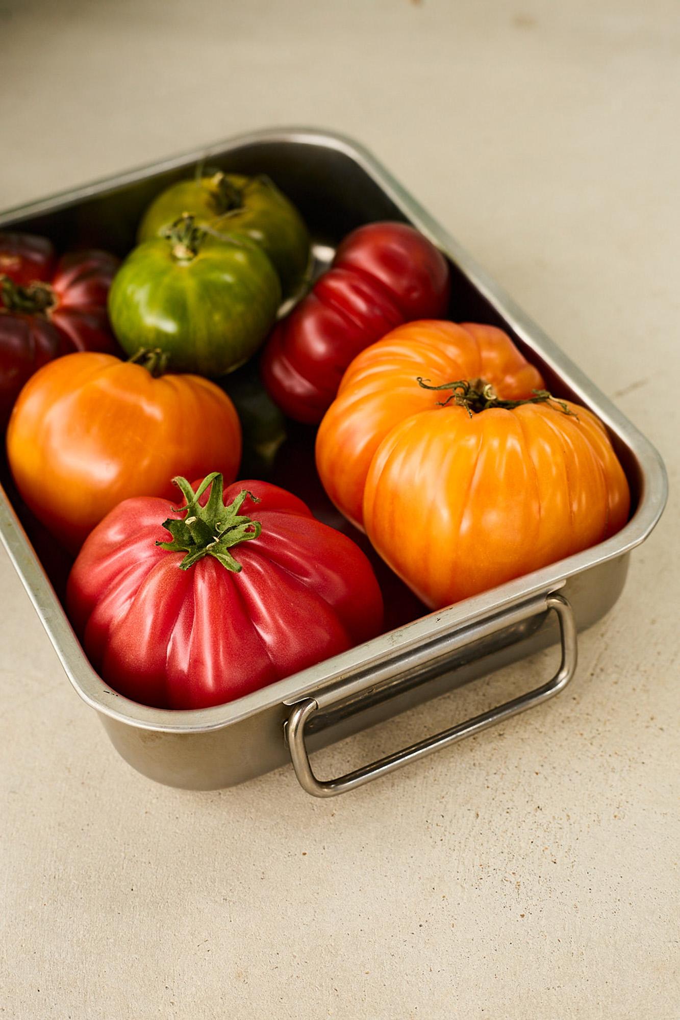 Fresh tomatoes in different colors arranged in a metal container.