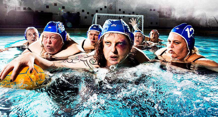 A group of people in a swimming pool, some wearing blue caps and others holding a yellow ball.