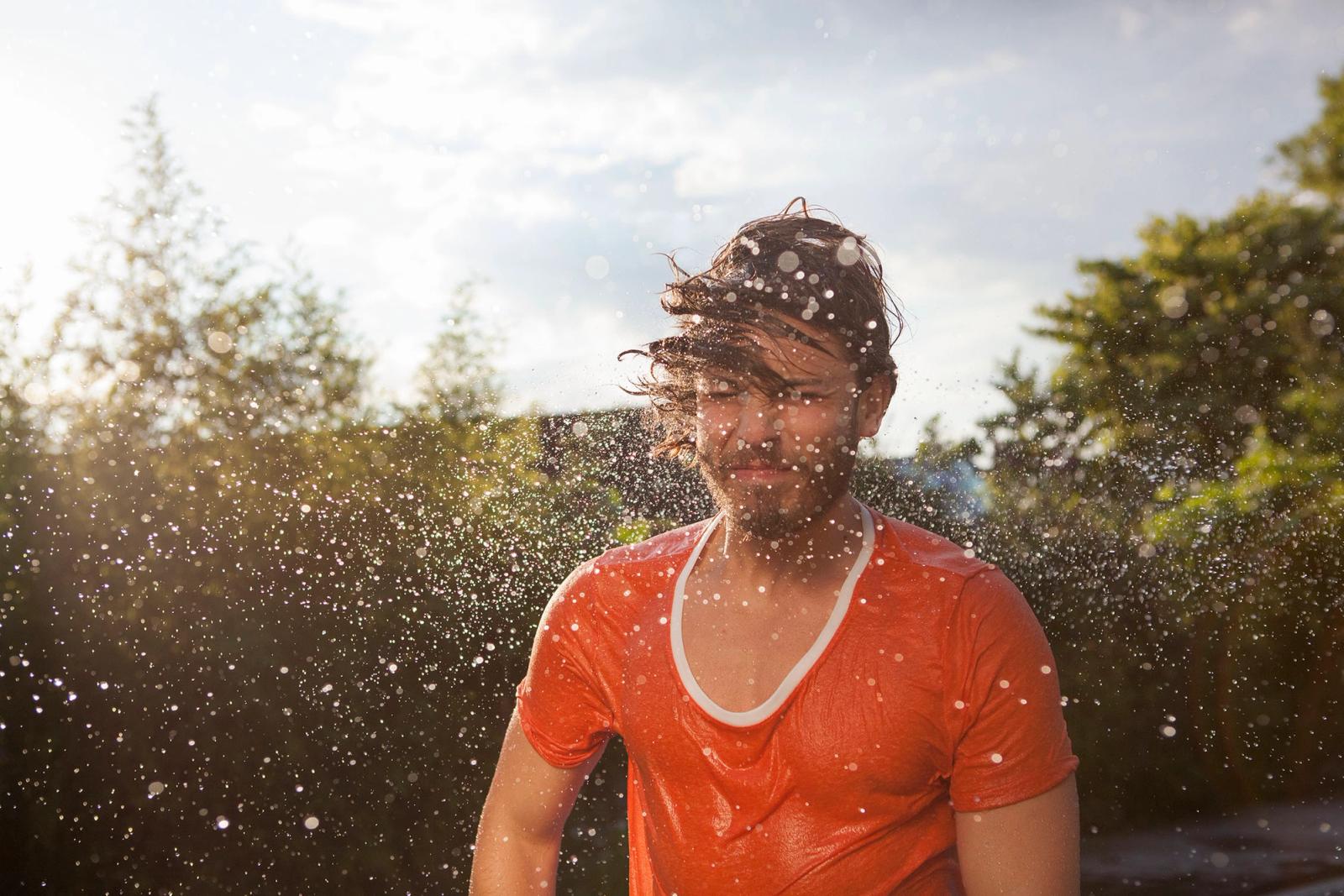 A man in a red t-shirt is getting sprayed with water, likely from a firehose or a water gun.