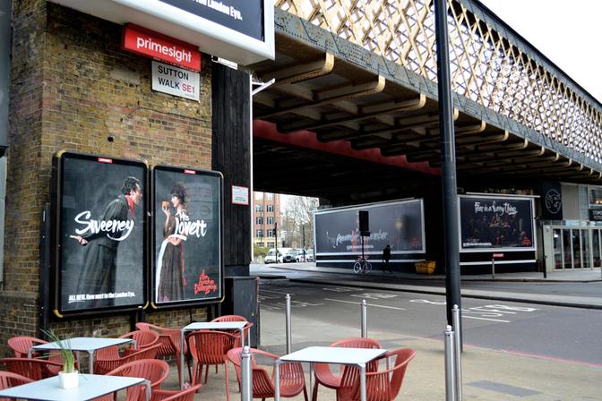 A London street with a billboard featuring a man and woman in 19th century clothing, standing in front of a London Dungeon billboard.