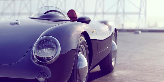 A classic, sleek, and futuristic sports car, possibly a 1950s or 1960s model, is parked in a modern, industrial-style setting, with a large, metal, industrial-style window or door in the background.