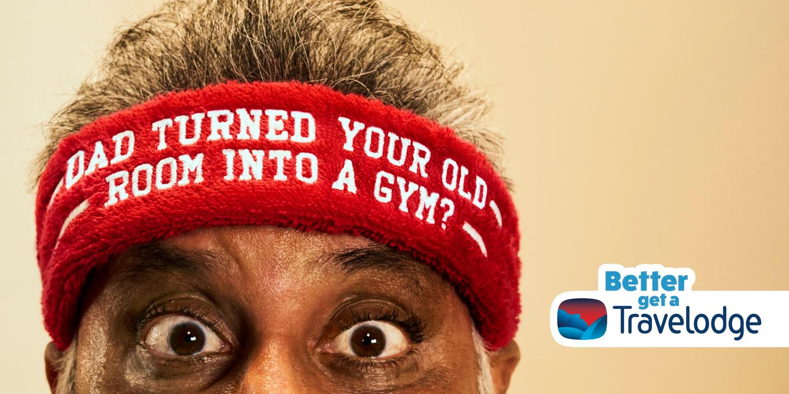 A man with a red headband with white text, looking directly at the camera with a mix of surprise and amusement. The headband reads "DAD TURNED YOUR OLD ROOM INTO A GYM?" in bold,.