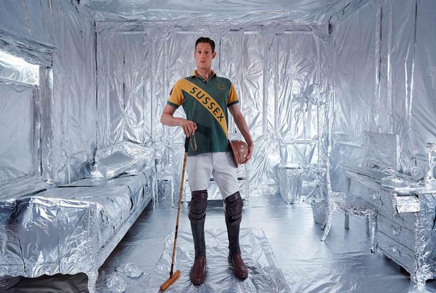 A man holds a polo mallet in a room with silver, foil-like walls and floor.