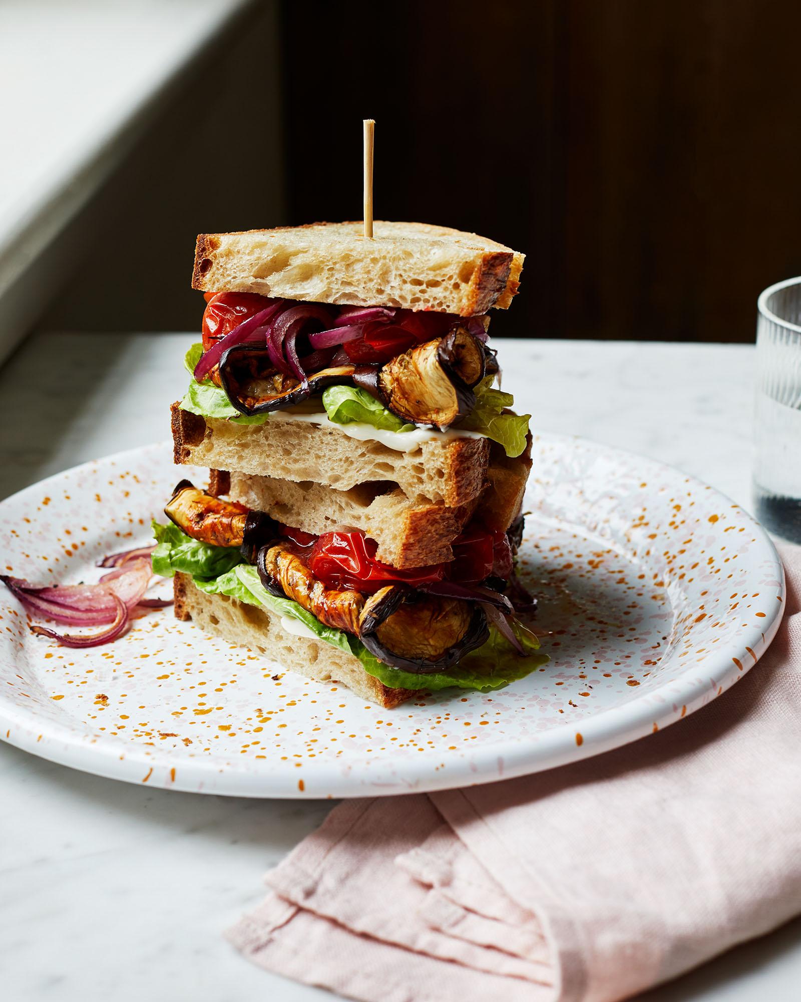 A sandwich with roasted vegetables, including eggplant, red onion, and tomatoes, on a white plate.