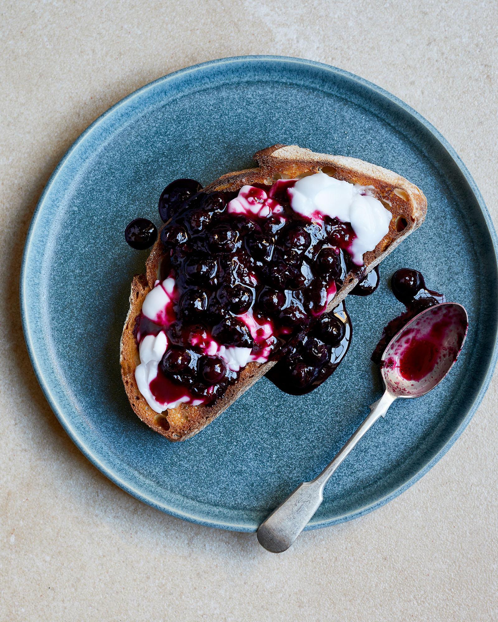 A slice of toast topped with blueberries and cream on a blue plate.