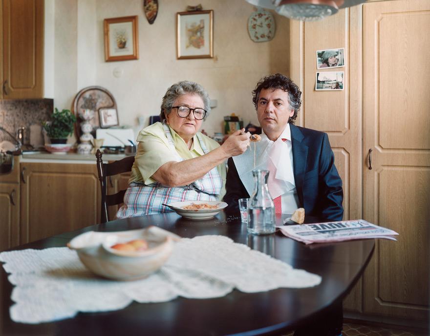 An older woman in a yellow shirt and a man in a suit sitting at a table eating spaghetti.