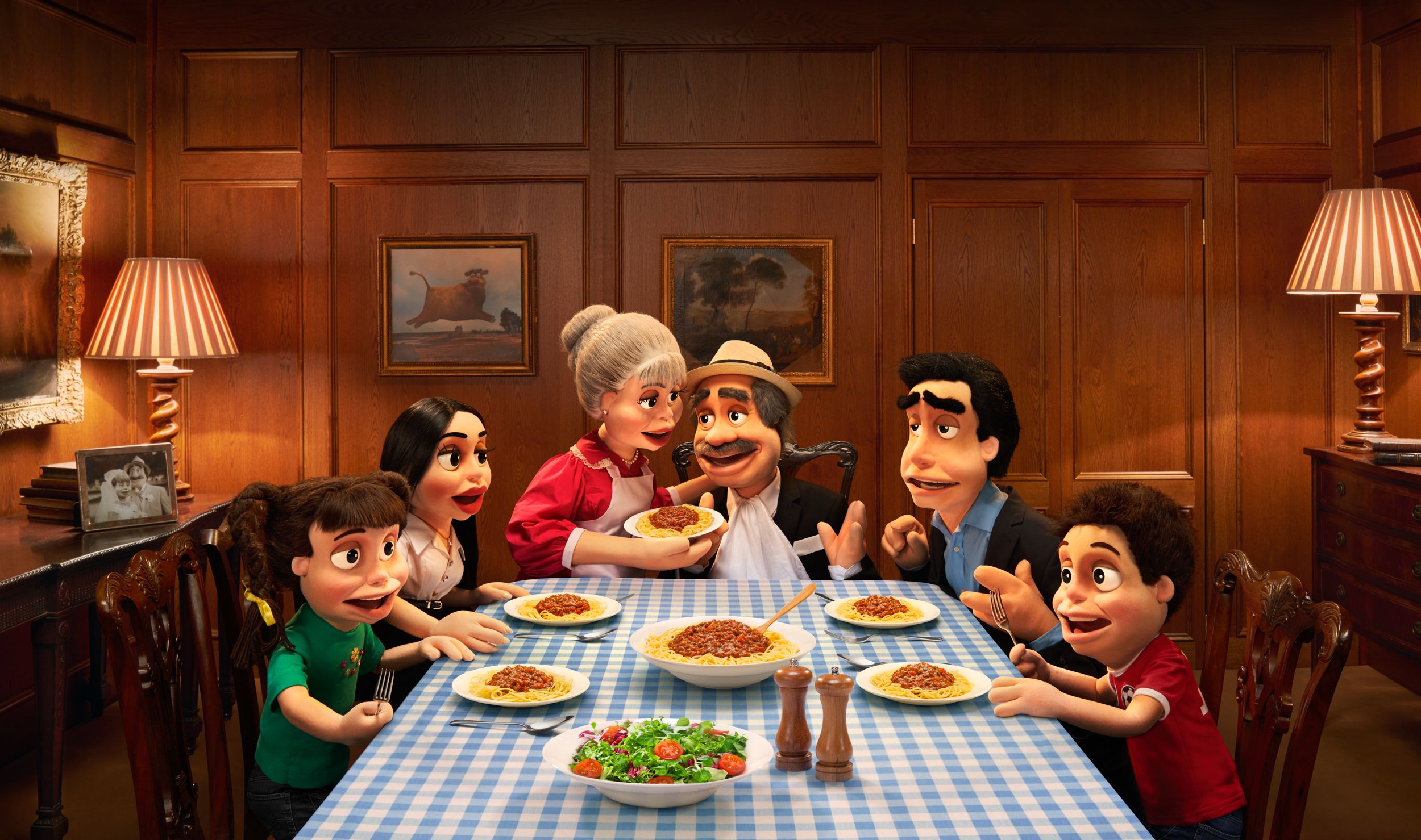 A group of anthropomorphic figures, including a chef, a teacher, a doctor, and a child, sit at a table eating spaghetti and salad.
