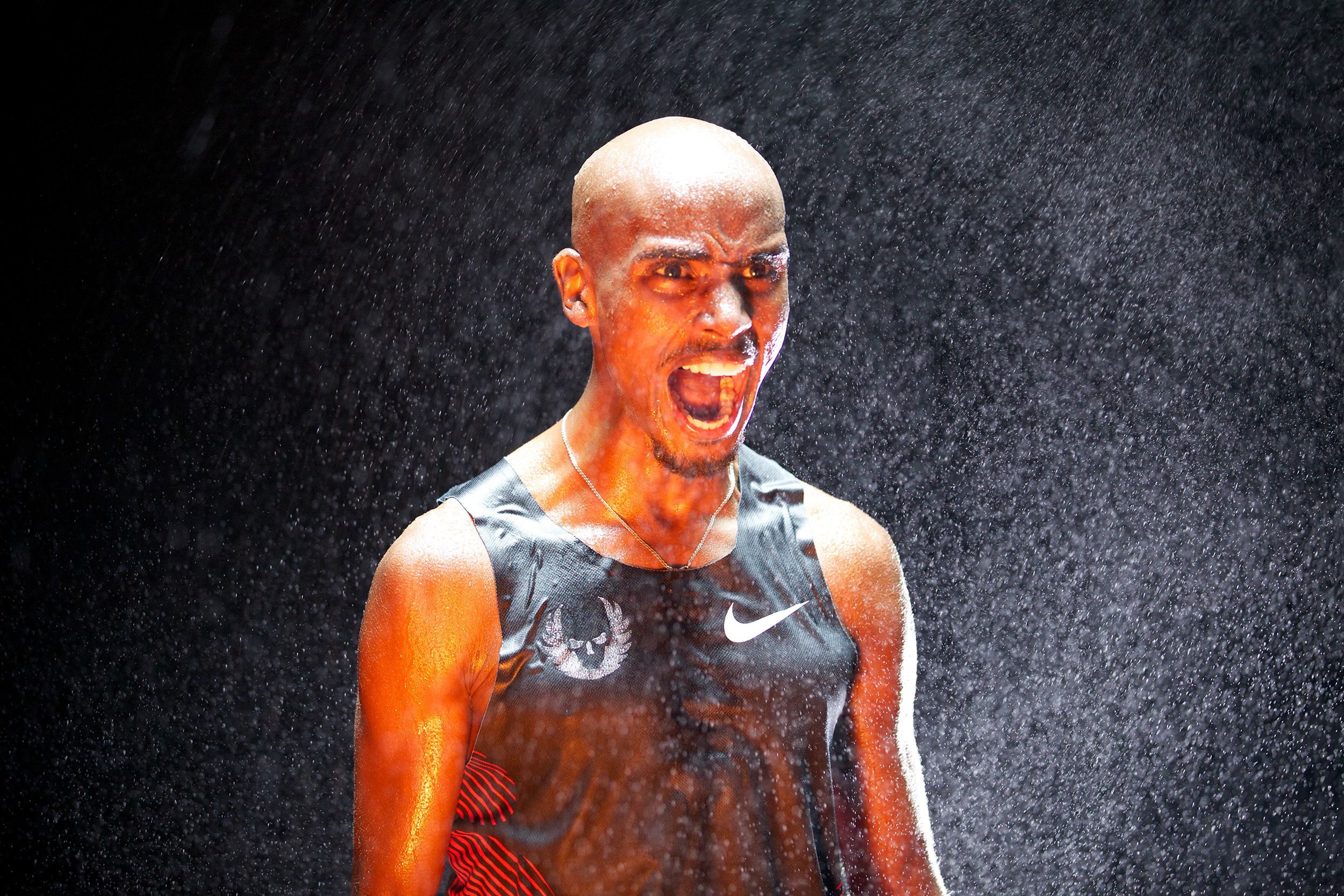A man with a shaved head and a black tank top with a white Nike swoosh logo is running in the rain, with water droplets on his face and a determined expression.