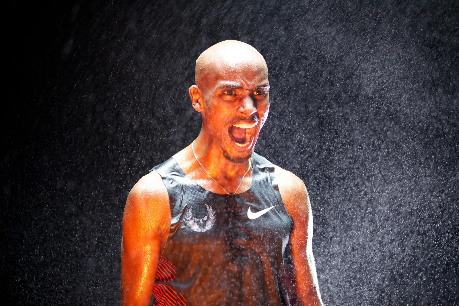 A man with a shaved head and a black tank top with a white Nike swoosh logo is running in the rain, with water droplets on his face and a determined expression.