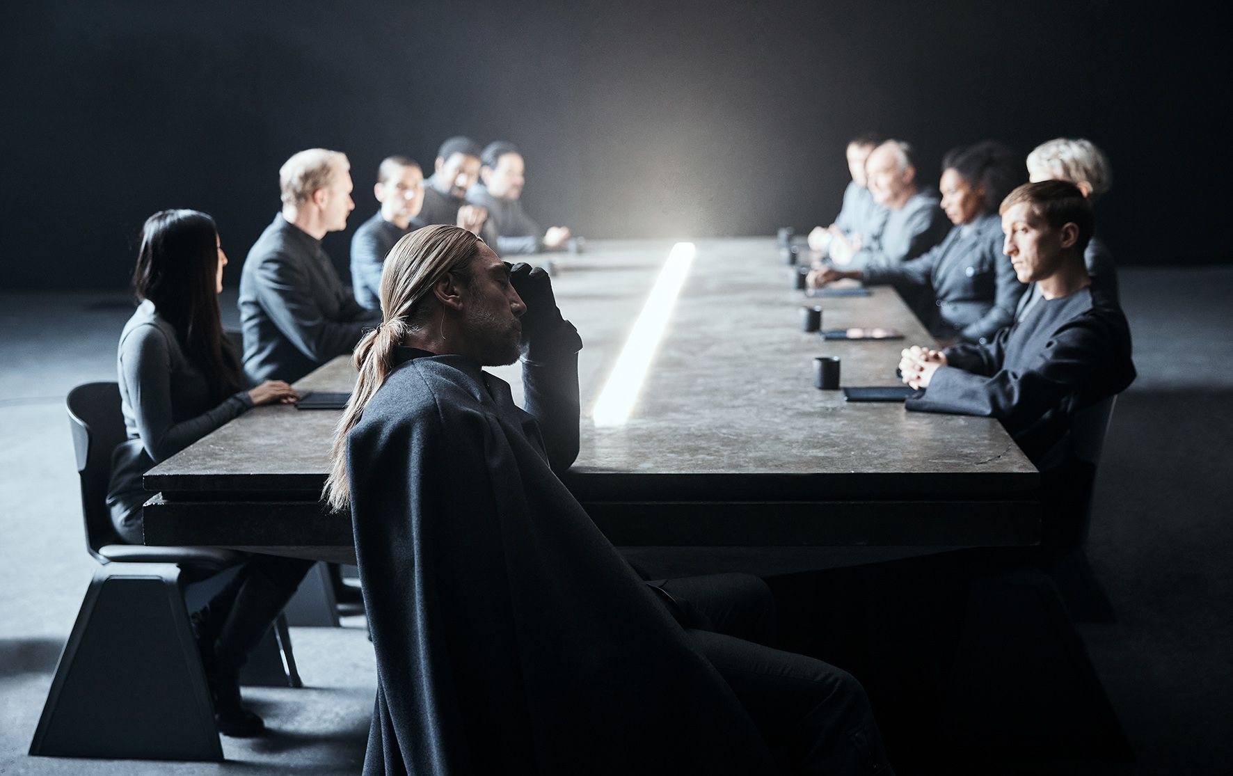 A group of people sit at a table while one looks out a window.