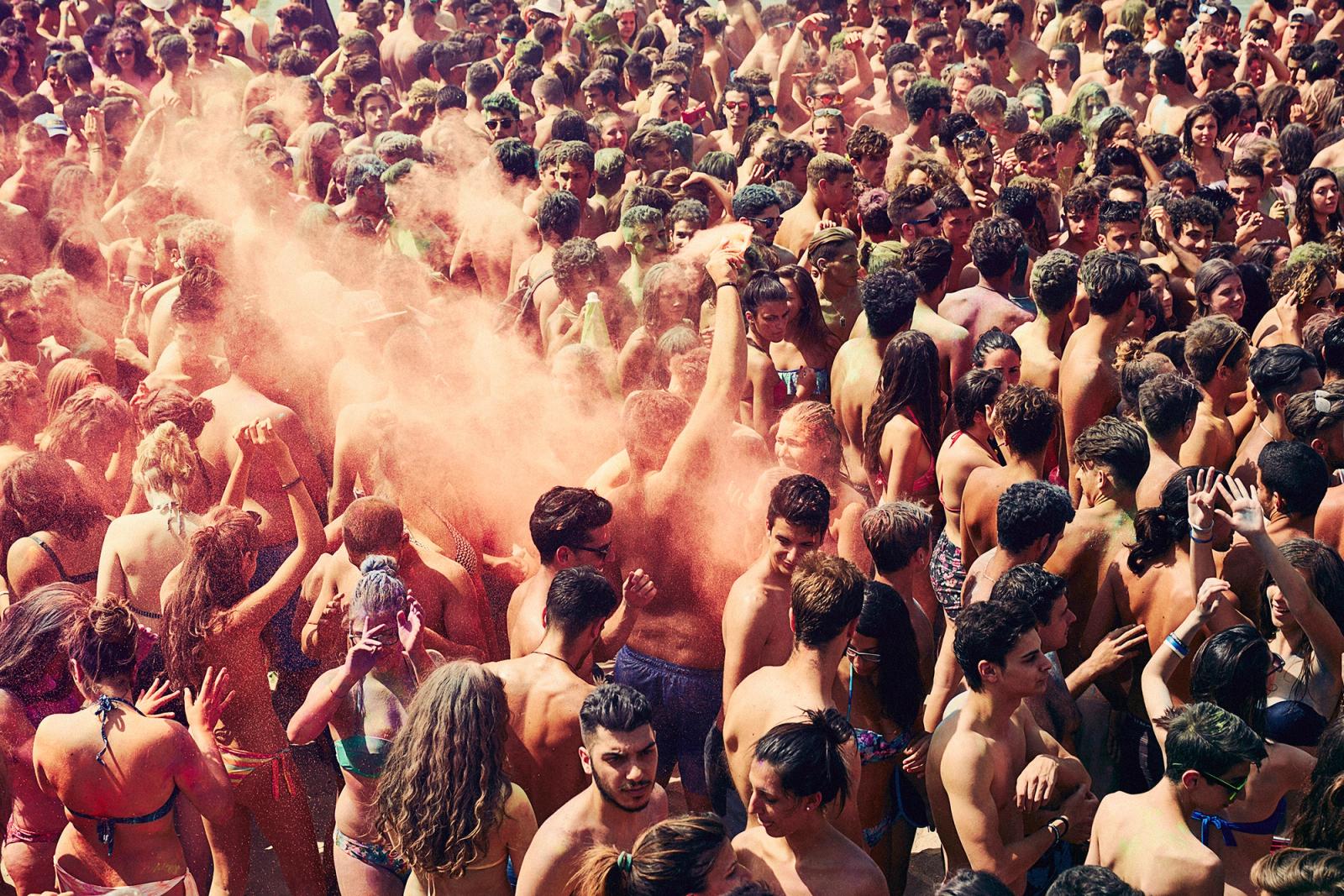 A crowd of people in a beach or pool area, likely at a music festival or party, with many people wearing swimsuits and some with beach or pool-related accessories.
