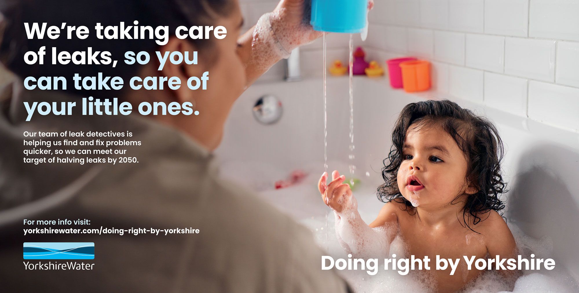 A woman in a white shirt is holding a blue bucket under a running faucet, with a child in the bathtub, playing with soap bubbles.