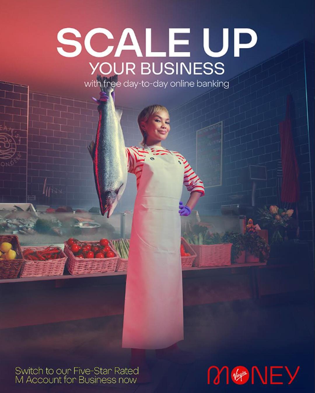 A woman in a white chef's coat and apron stands in a kitchen, holding up a large fish.