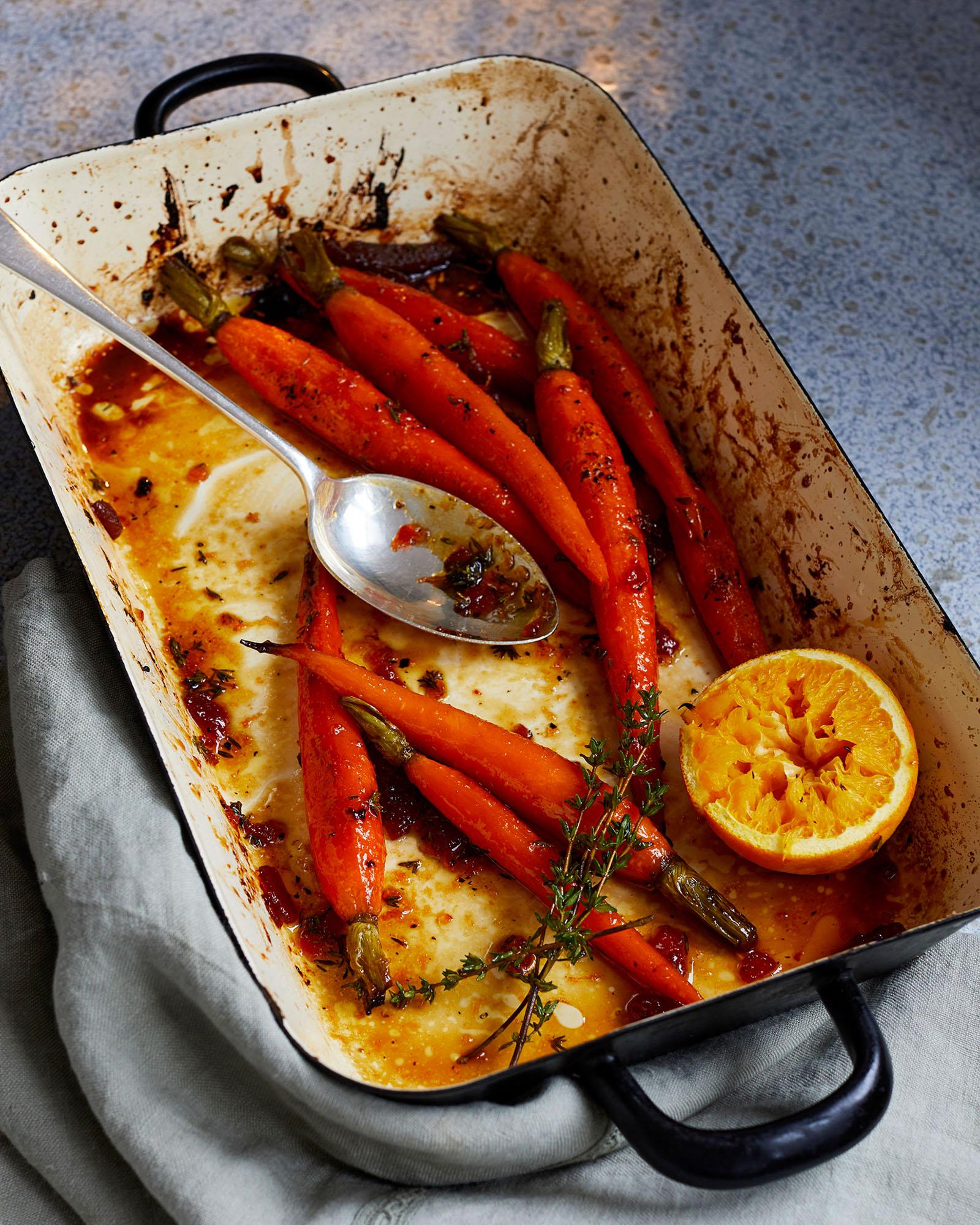 A baking dish containing roasted carrots with a mixture of herbs and a slice of orange, possibly served as a side dish or part of a larger meal.