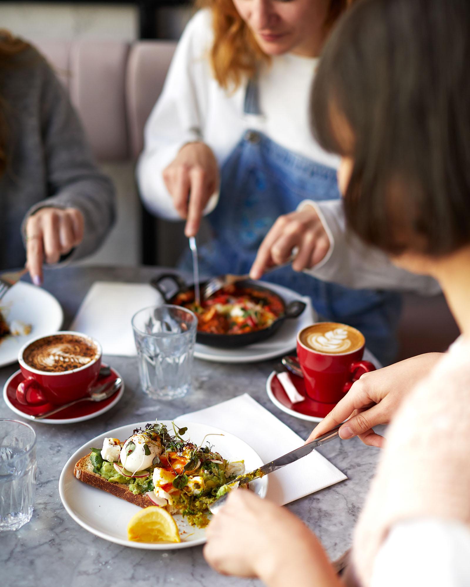 A group of people eating a meal at a table, with multiple plates of food and several cups of coffee or other beverages.