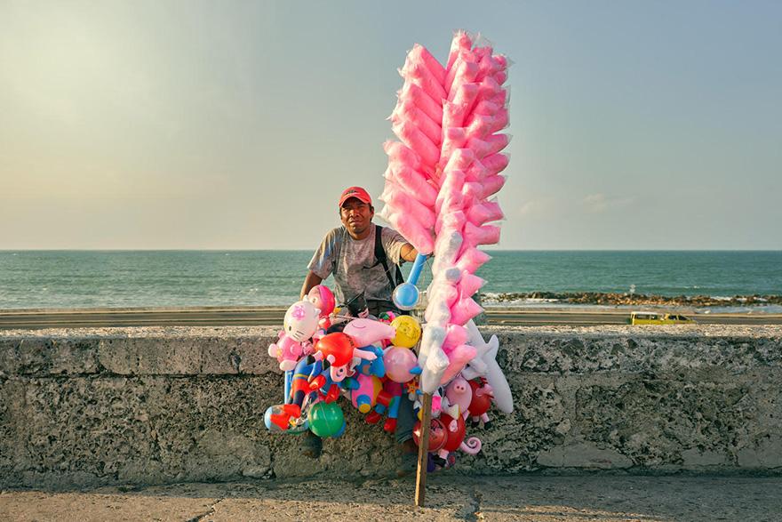 A man sits on a wall near the sea with toys and cotton candy nearby.