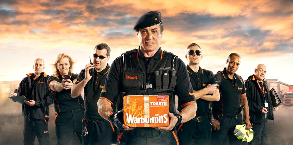 A group of uniformed individuals standing in front of a fire station, holding equipment and a box of Warburton's toast.
