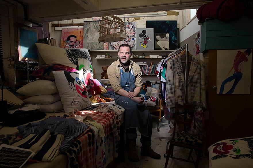 A man working in a studio surrounded by art pieces and clothing.