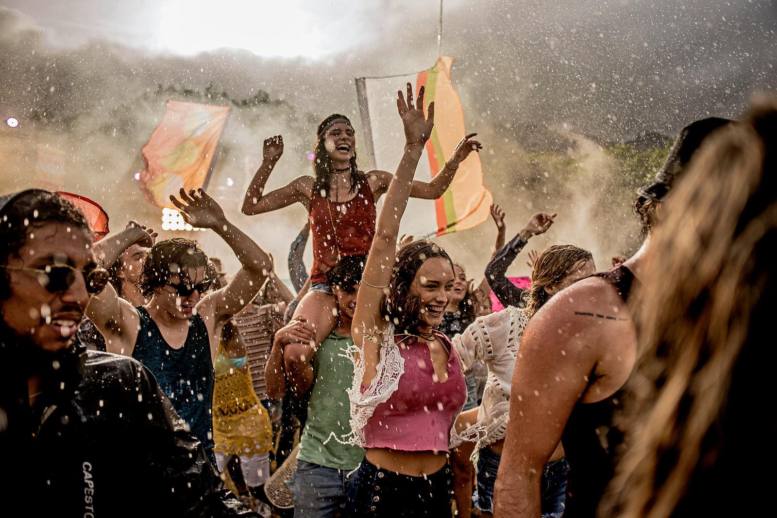 A crowd of people dancing and celebrating in the rain, with some people holding umbrellas and others dancing with their arms raised.