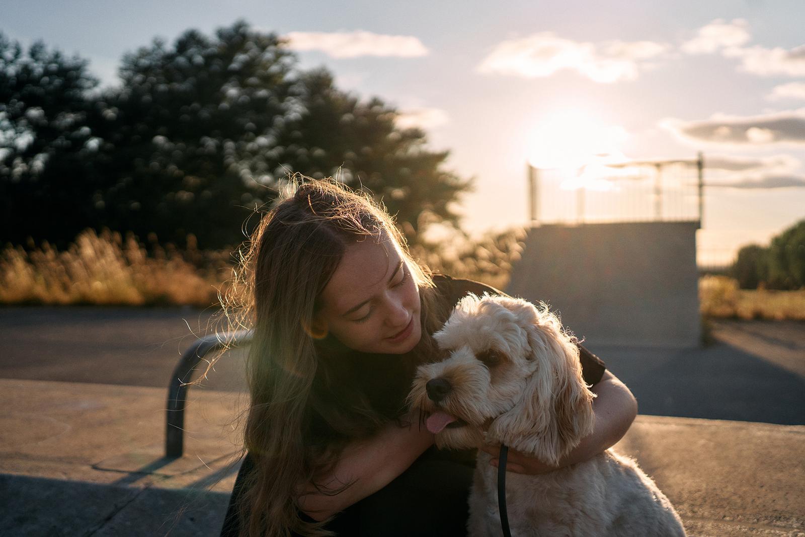 A woman is hugging a small, fluffy, white dog with a brown nose and ears.