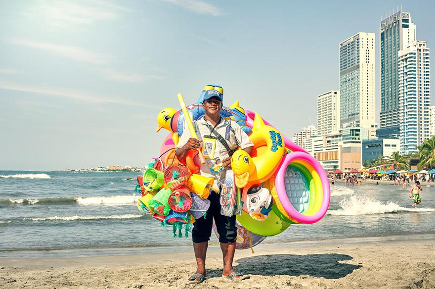 A street vendor on a beach selling various colorful inflatables.