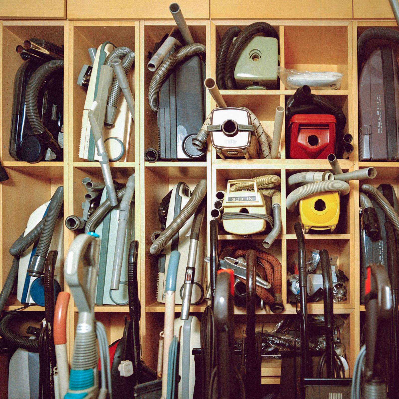 A collection of vintage and modern vacuum cleaners on shelves.