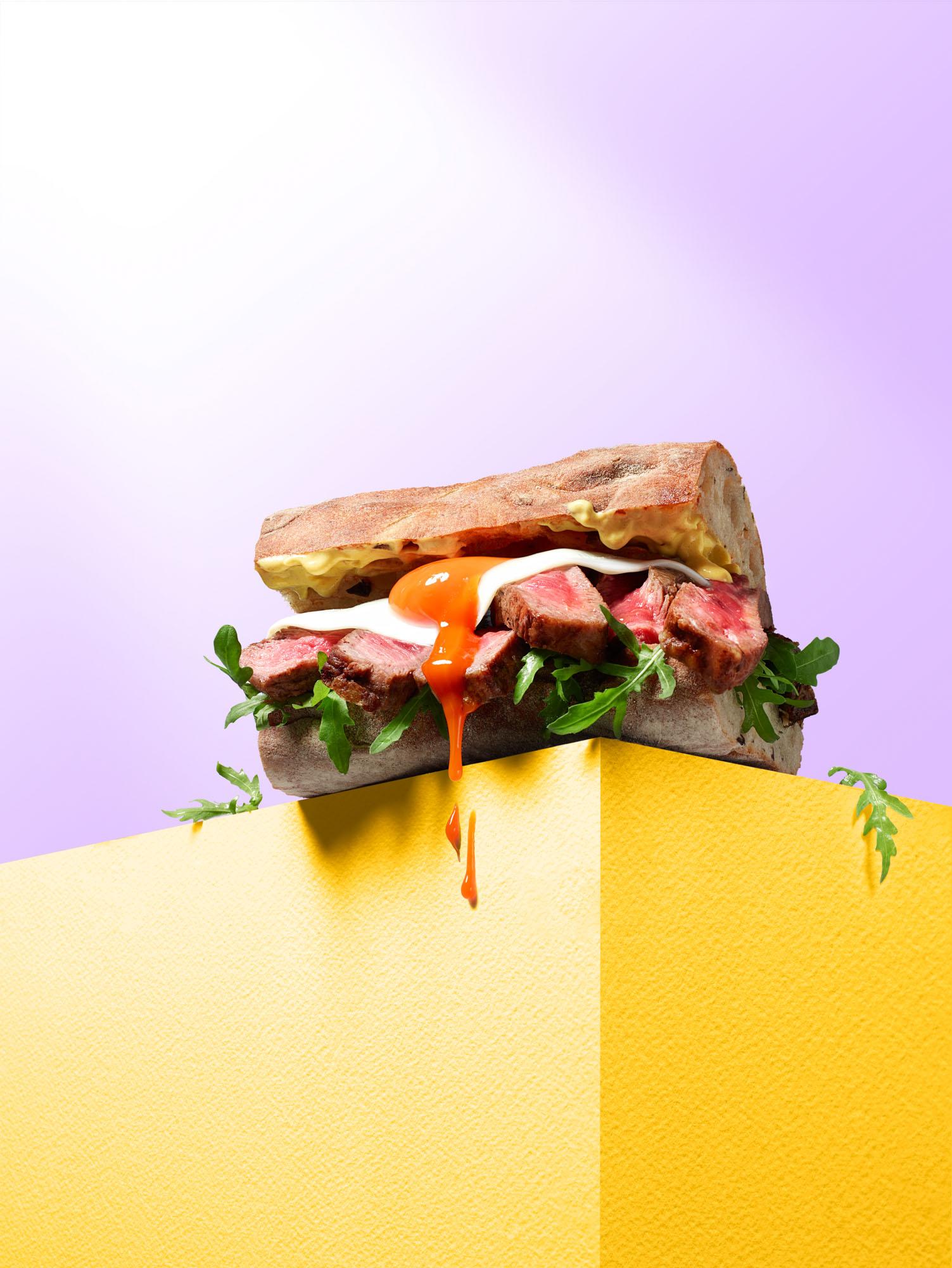 A sandwich with steak, egg, and arugula on toasted bread, served on a yellow plate.