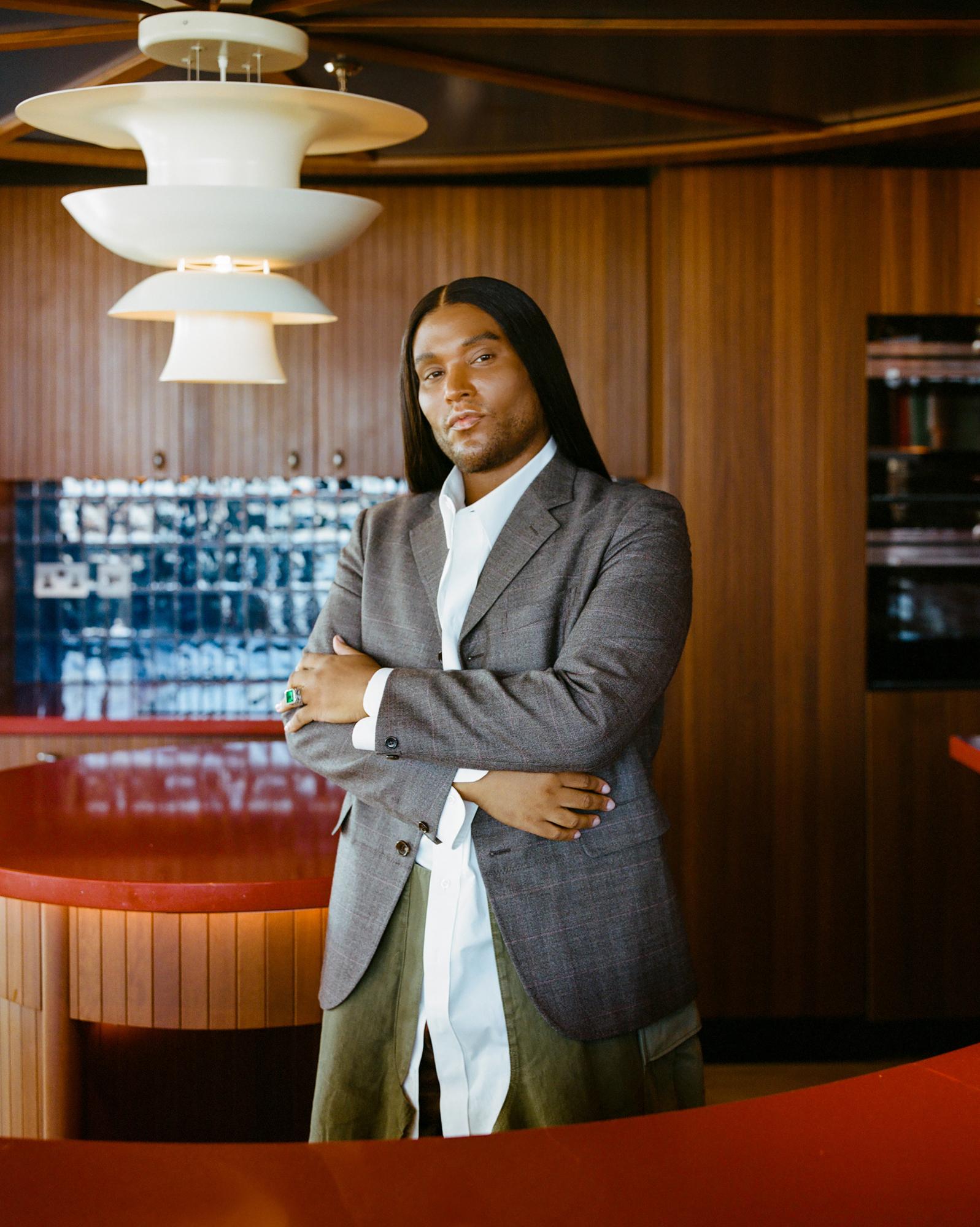 A man stands in a modern, wood-paneled room with a red counter and a large, white light fixture.