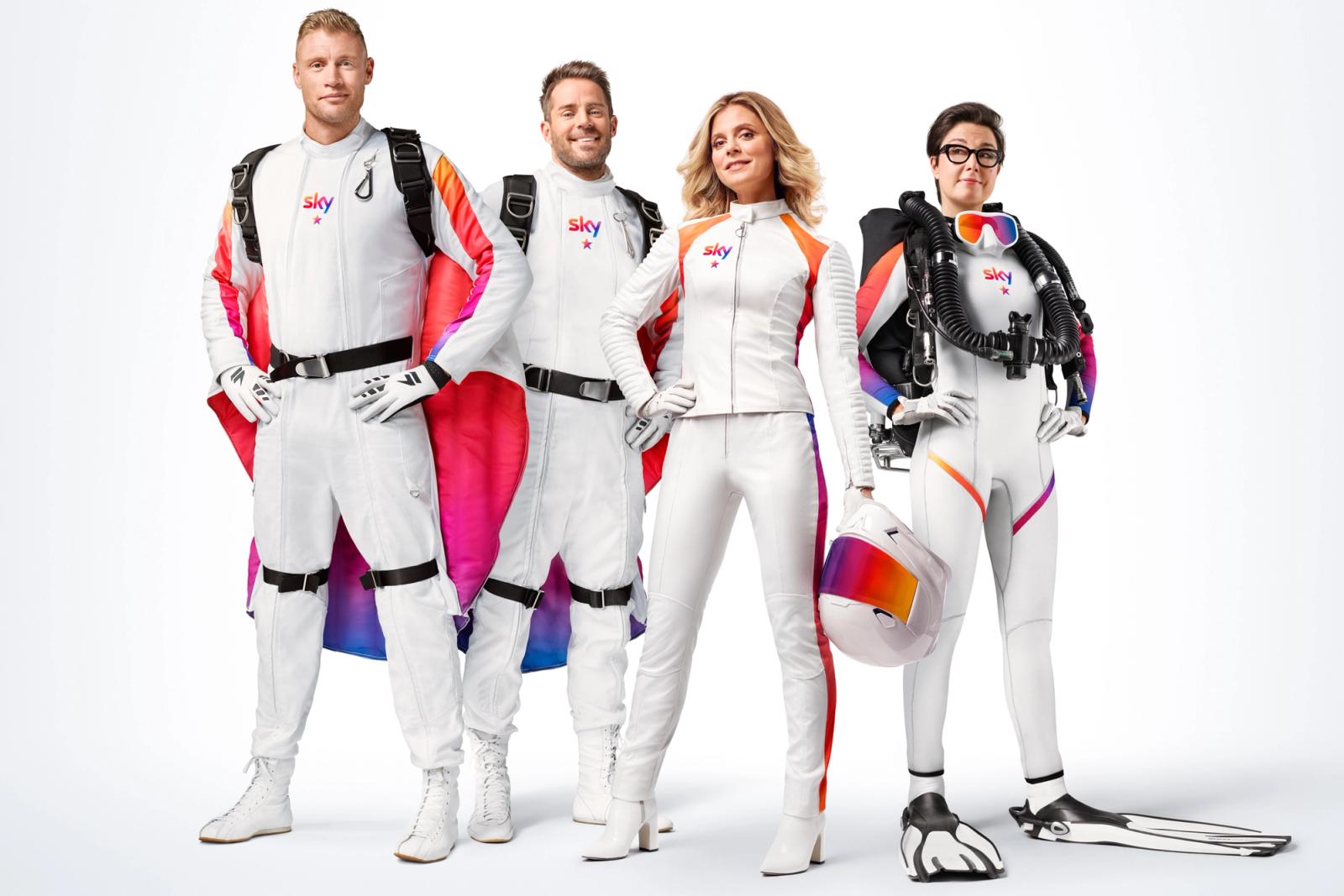 Four people in white and red skydiving suits, one with a scuba diving tank, and another with a helmet.