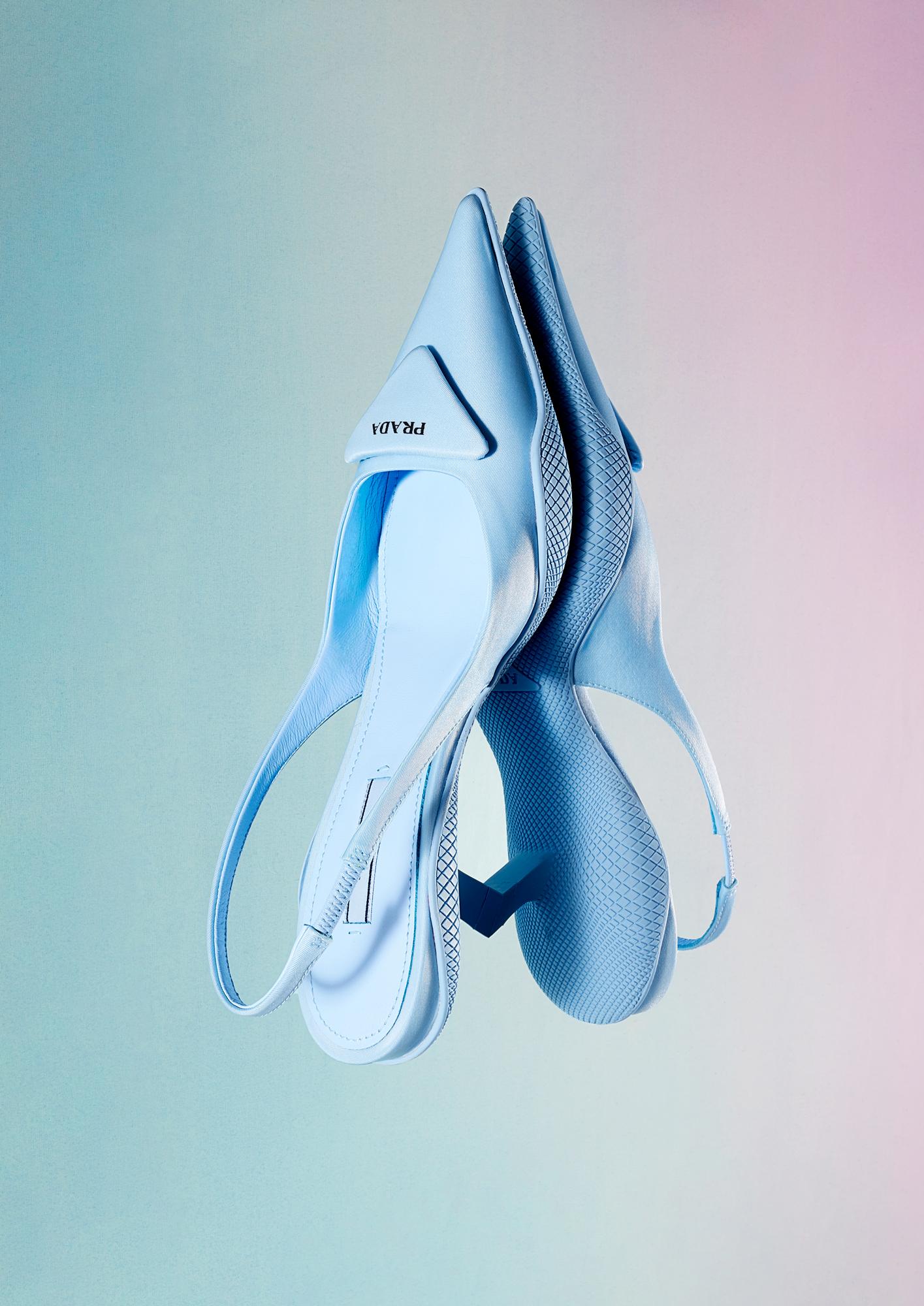 A pair of high-heeled, pointed-toe, patent leather, sling-back shoes, likely made by Prada.