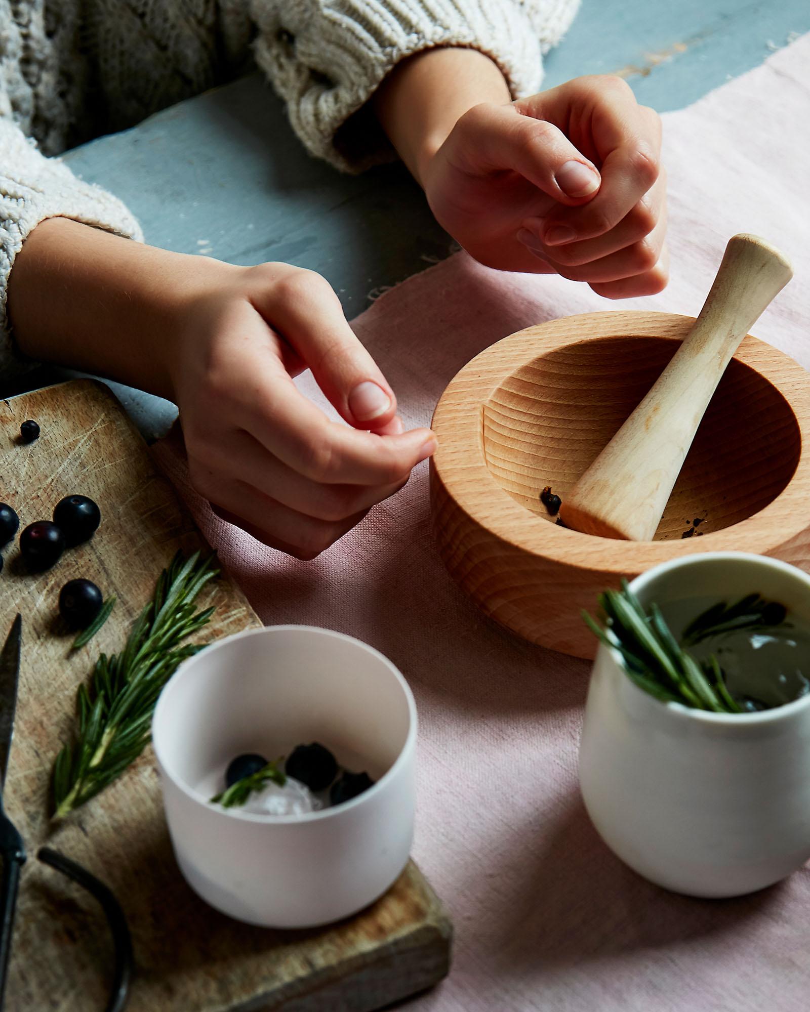 A person's hands are shown in the foreground, with a mortar and pestle in the background, surrounded by various herbs and spices.