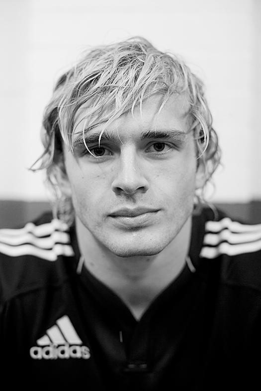 A young man with a messy, wet, and slightly long hair, wearing a black and white Adidas football jersey.