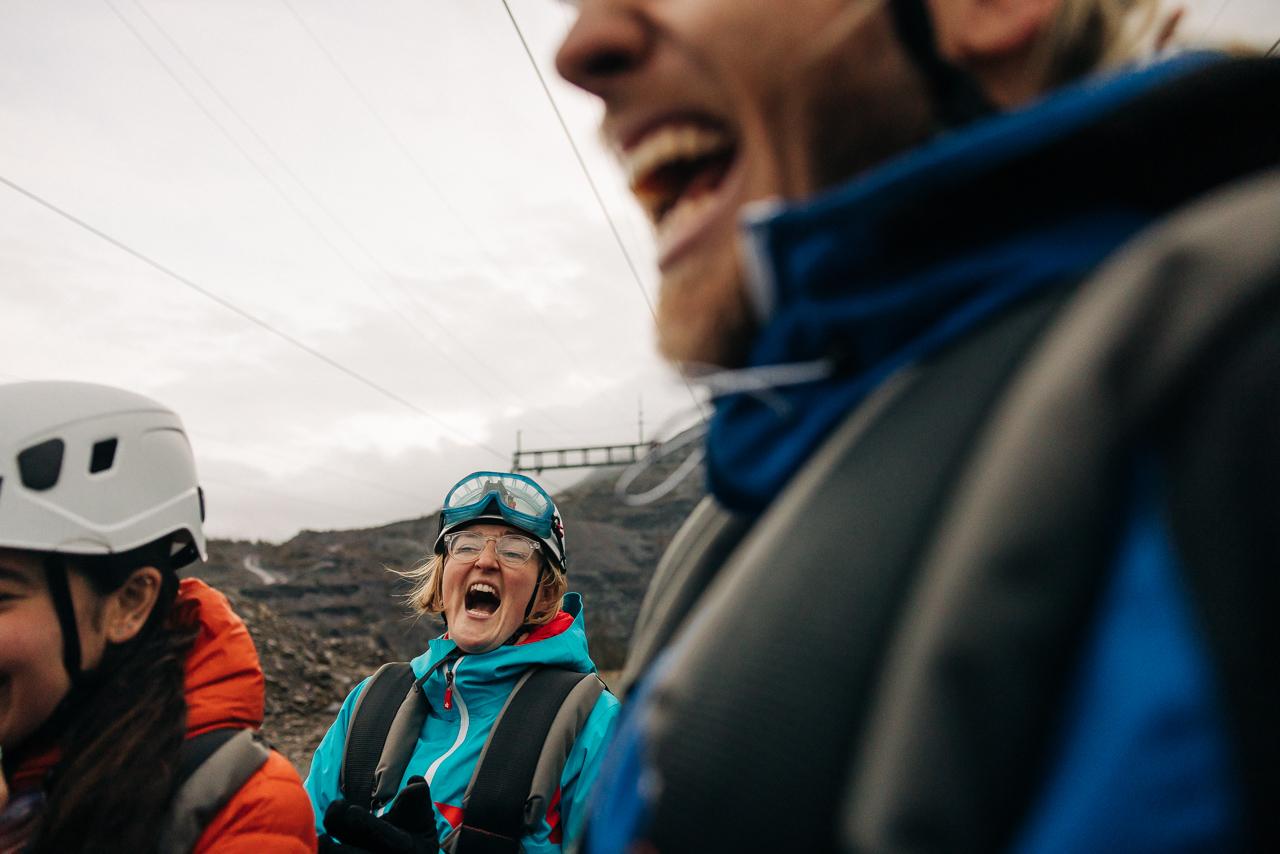 A woman in a blue jacket and helmet, laughing with others in a rugged, rocky landscape.