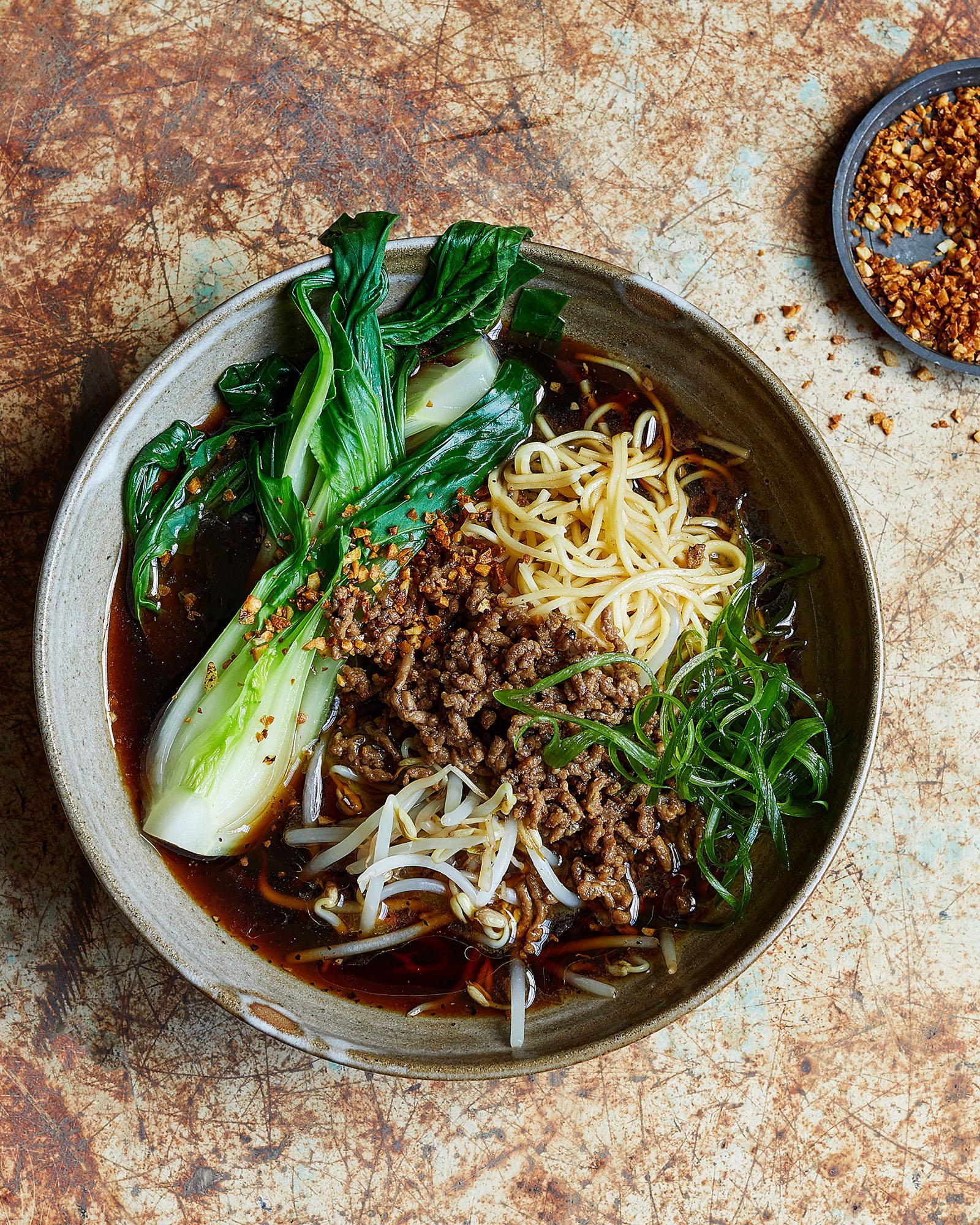 A bowl of noodles with beef, bok choy, and noodles in a savory broth, served in a ceramic bowl on a wooden table.