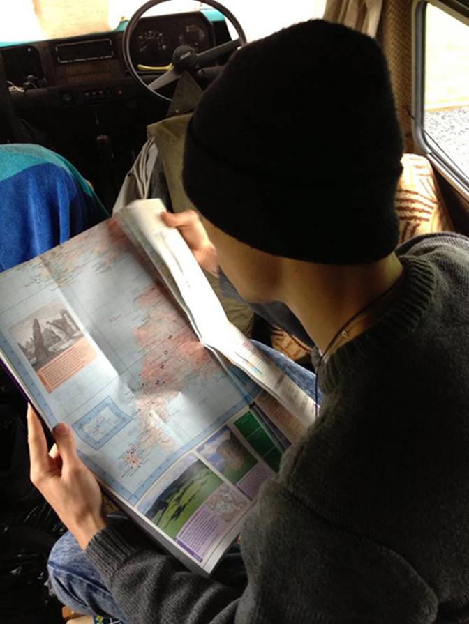 A person is sitting in the driver's seat of a vehicle, holding a map and looking at it.