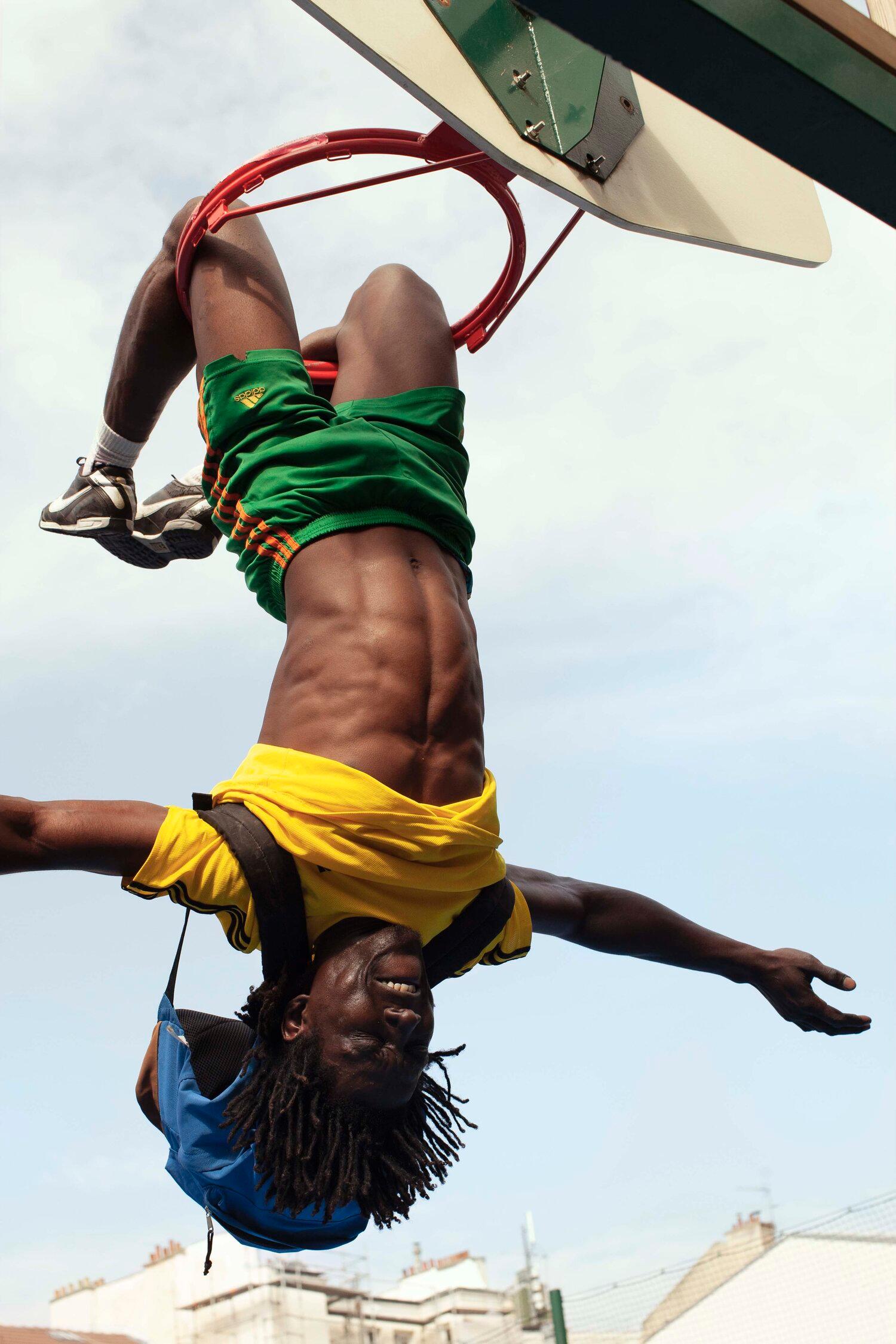 A person is doing a backflip on a trampoline, wearing a yellow and green football jersey, with a city skyline in the background.