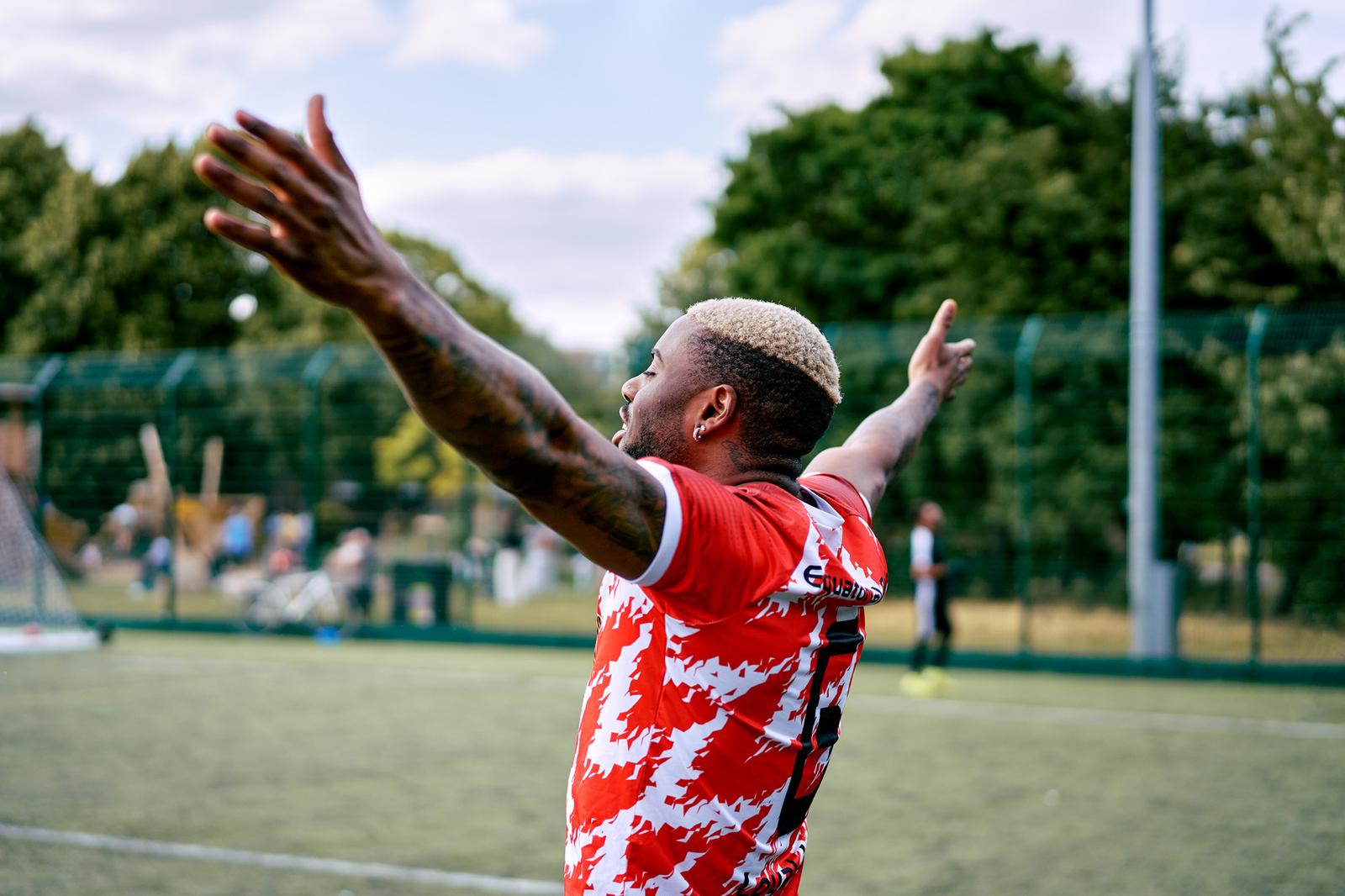 A man with his arms outstretched, wearing a red and white football jersey, on a football field.