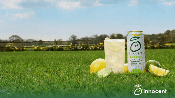 A can of Innocent Bubbles, a lemon-flavored drink, sitting on a grassy lawn with a few lemons and a glass of the drink in the background.