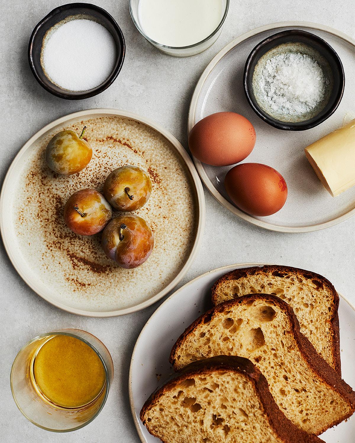 A selection of food and ingredients, including bread, eggs, cheese, and fruit, on a table or counter.