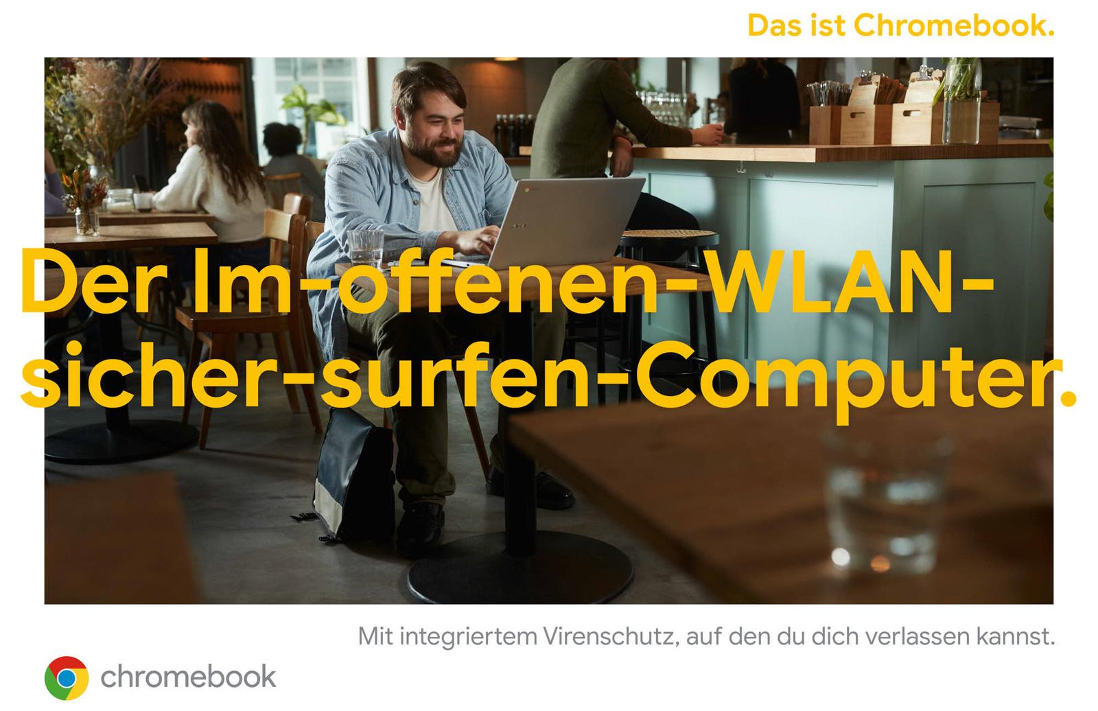 A man with a beard and glasses, wearing a light blue button-down shirt and dark pants, sits at a small table in a restaurant or café. He is using a laptop, which is open on the.