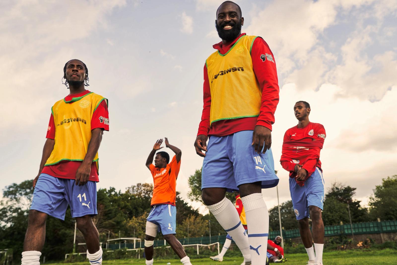 A group of football players in a field, wearing football jerseys and shorts, with one player in the foreground wearing a yellow bib.